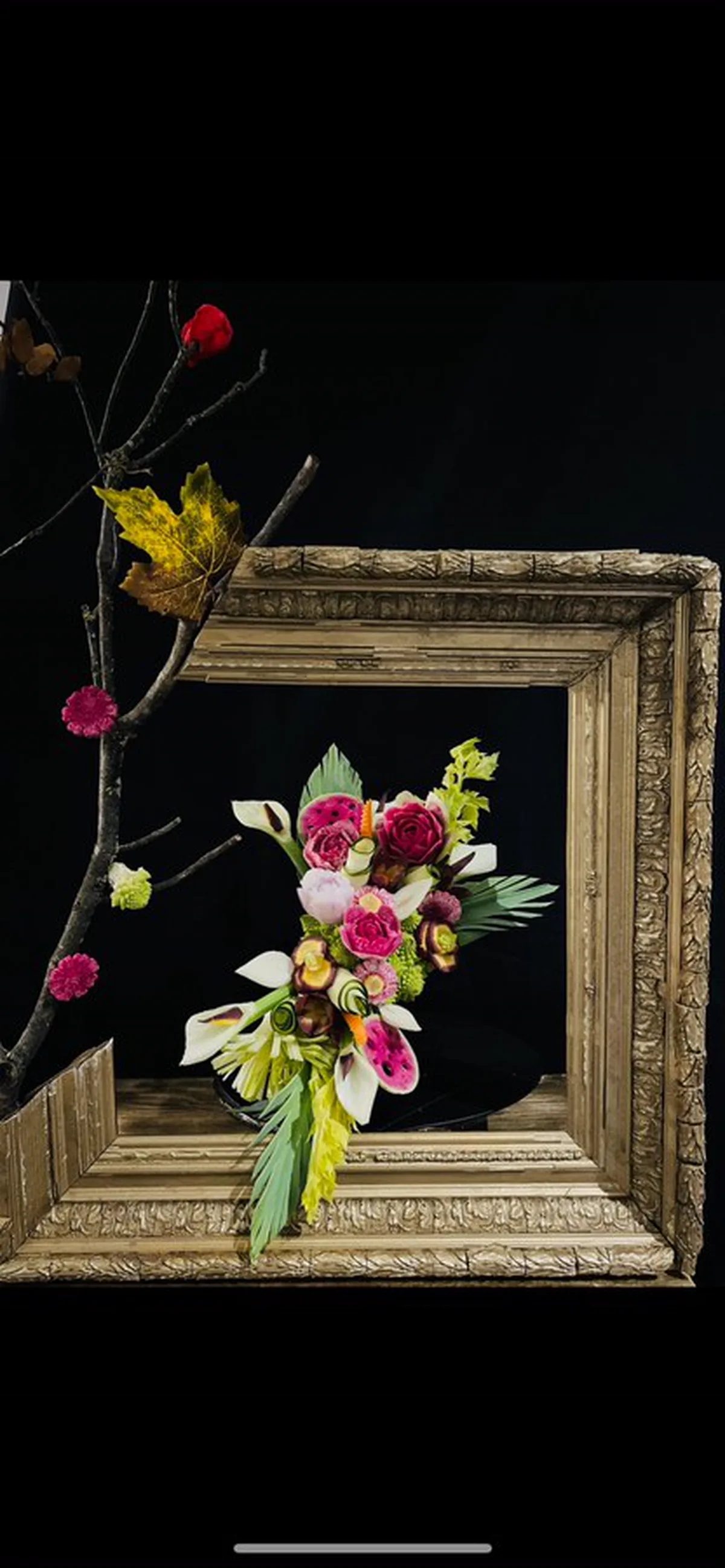 Composition de fleurs sculptées dans des légumes, débordant d’un cadre ancien doré.