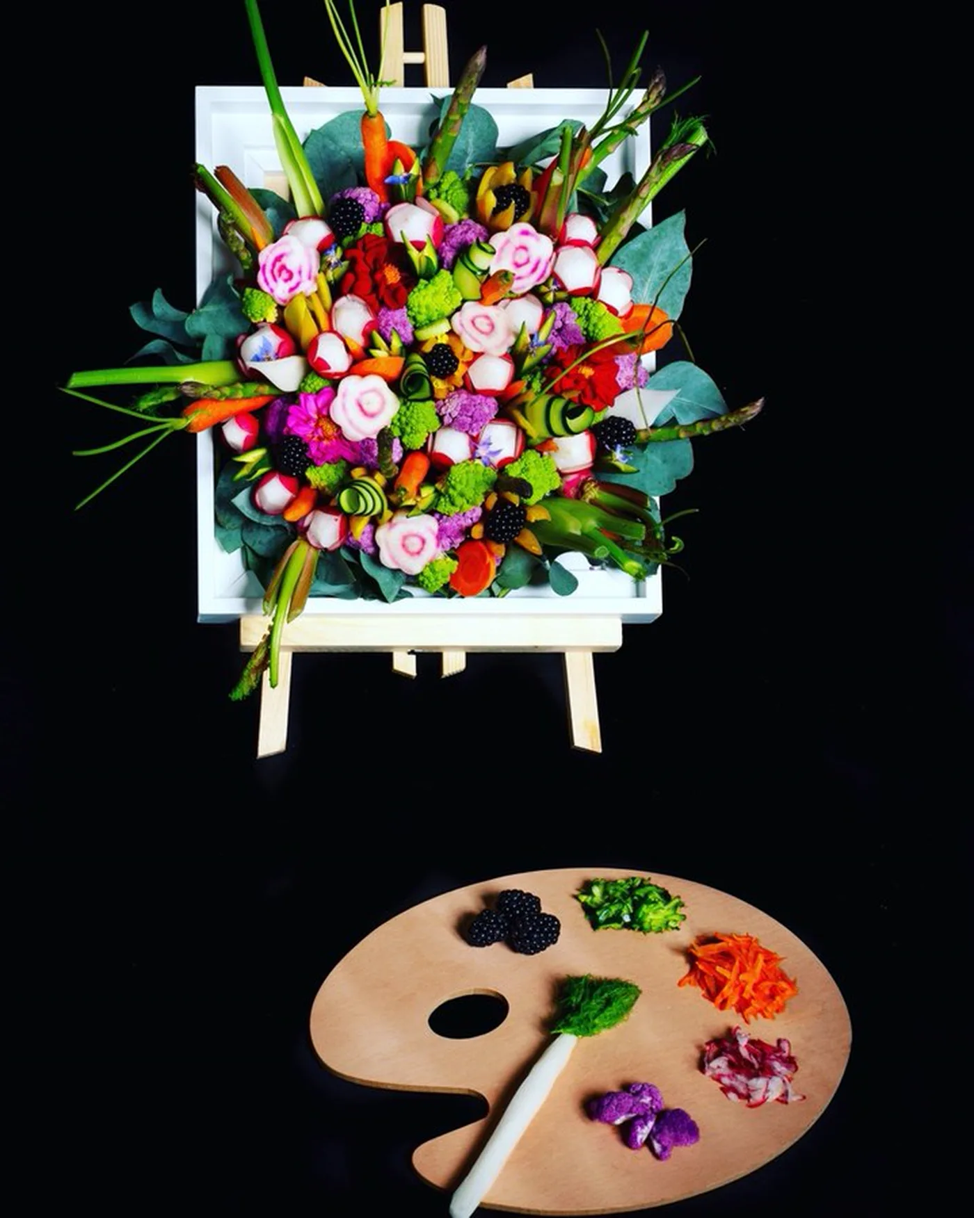 Corbeille de légumes sculptés dans un cadre blanc sur un chevalet de peintre.