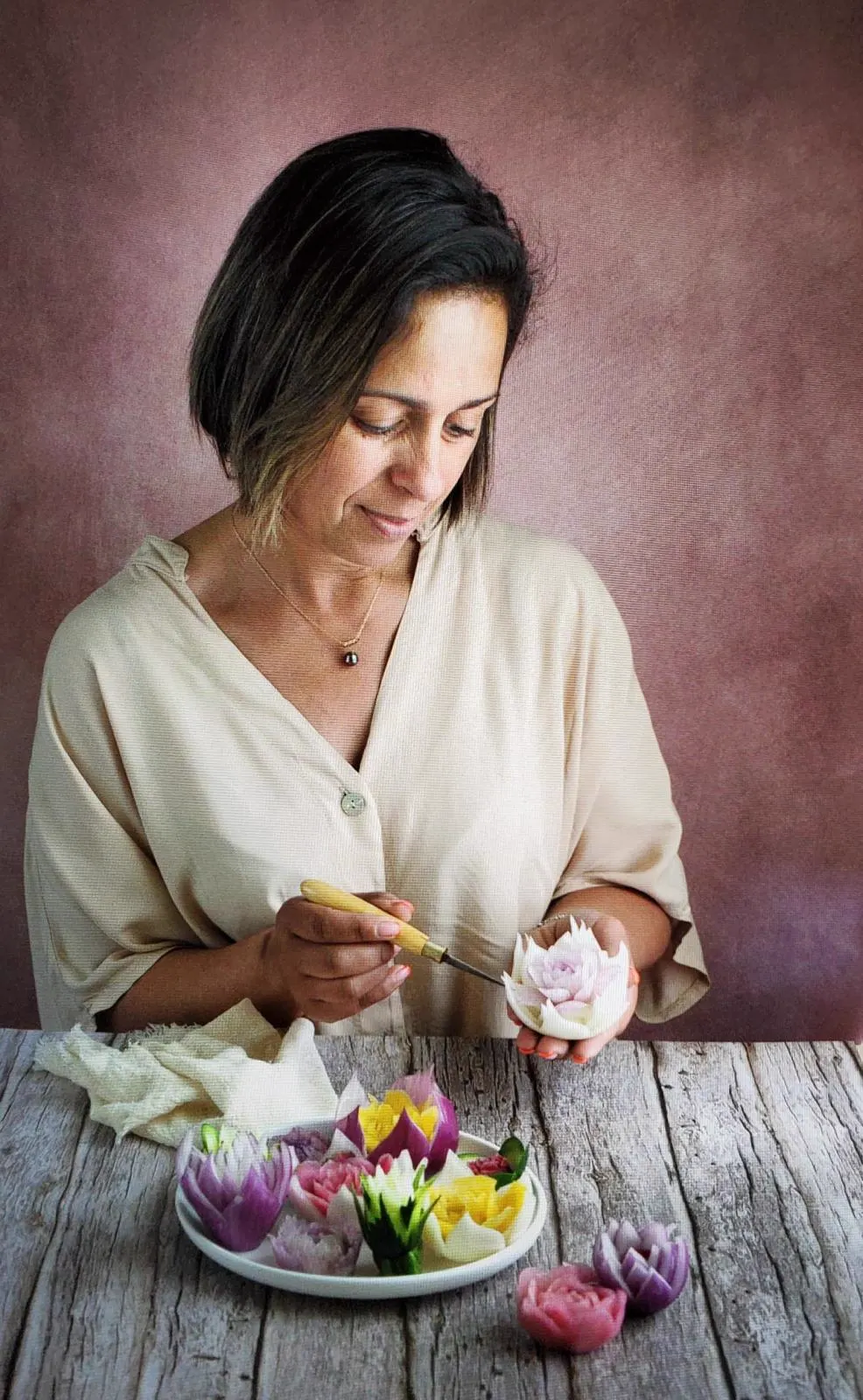 Samira Lemaire sculptant une fleur au couteau, entourée de ses créations sur une assiette.